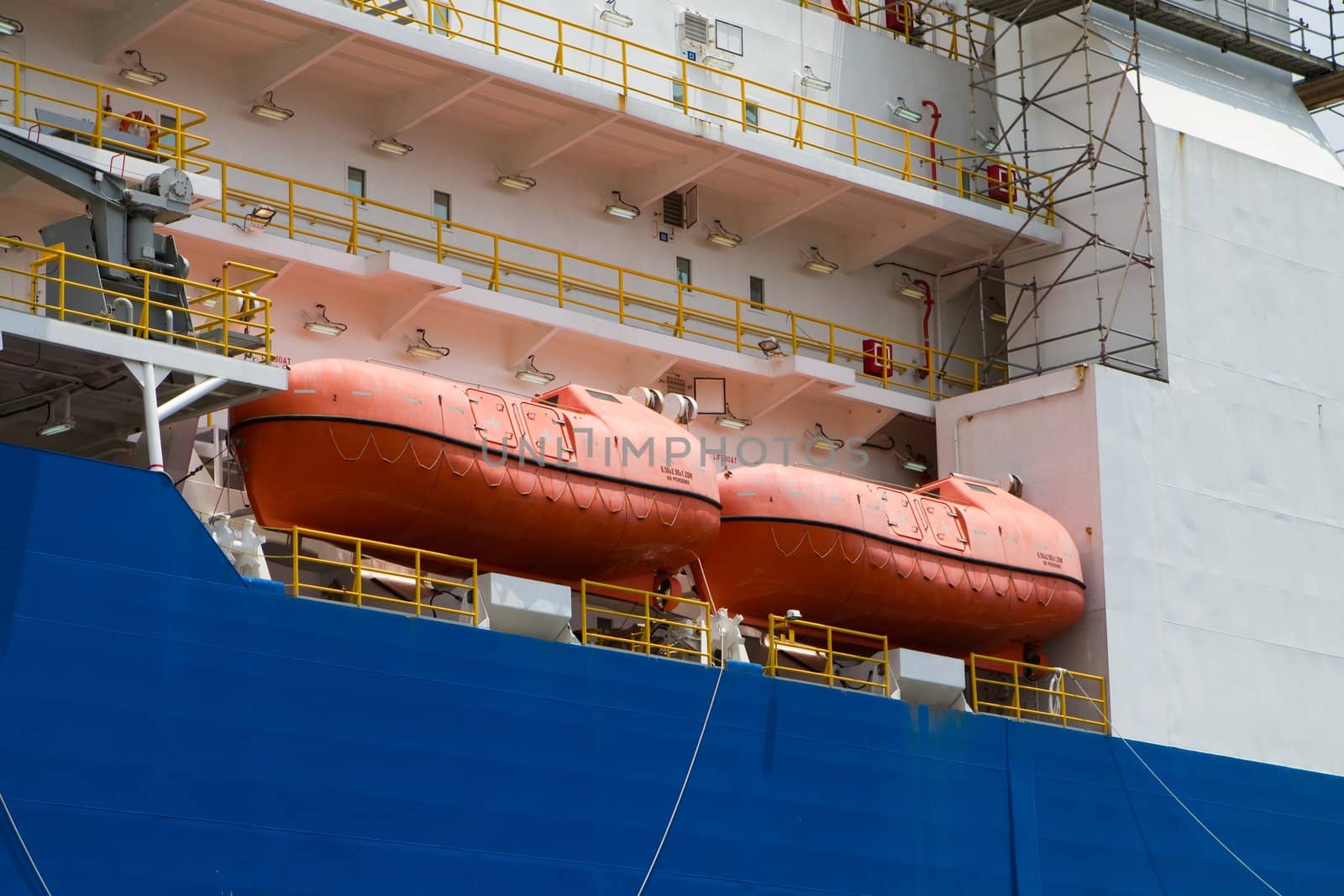 Orange survival lifeboats sit on the deck of an industrial ship.