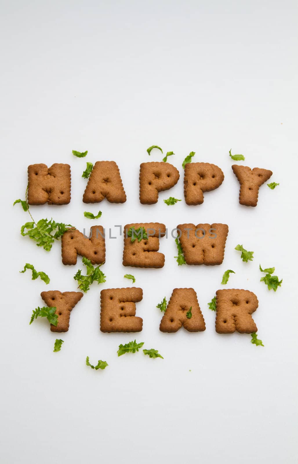 Happy New Year greeting words made by brown biscuits with green leaves on white surface in portrait orientation for background use