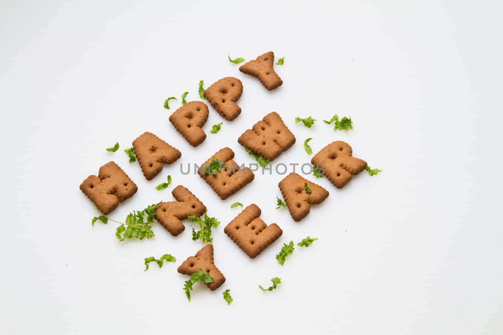 Angled view of Happy New Year greeting words made by brown biscuits with green leaves on white surface in landscape orientation for background use