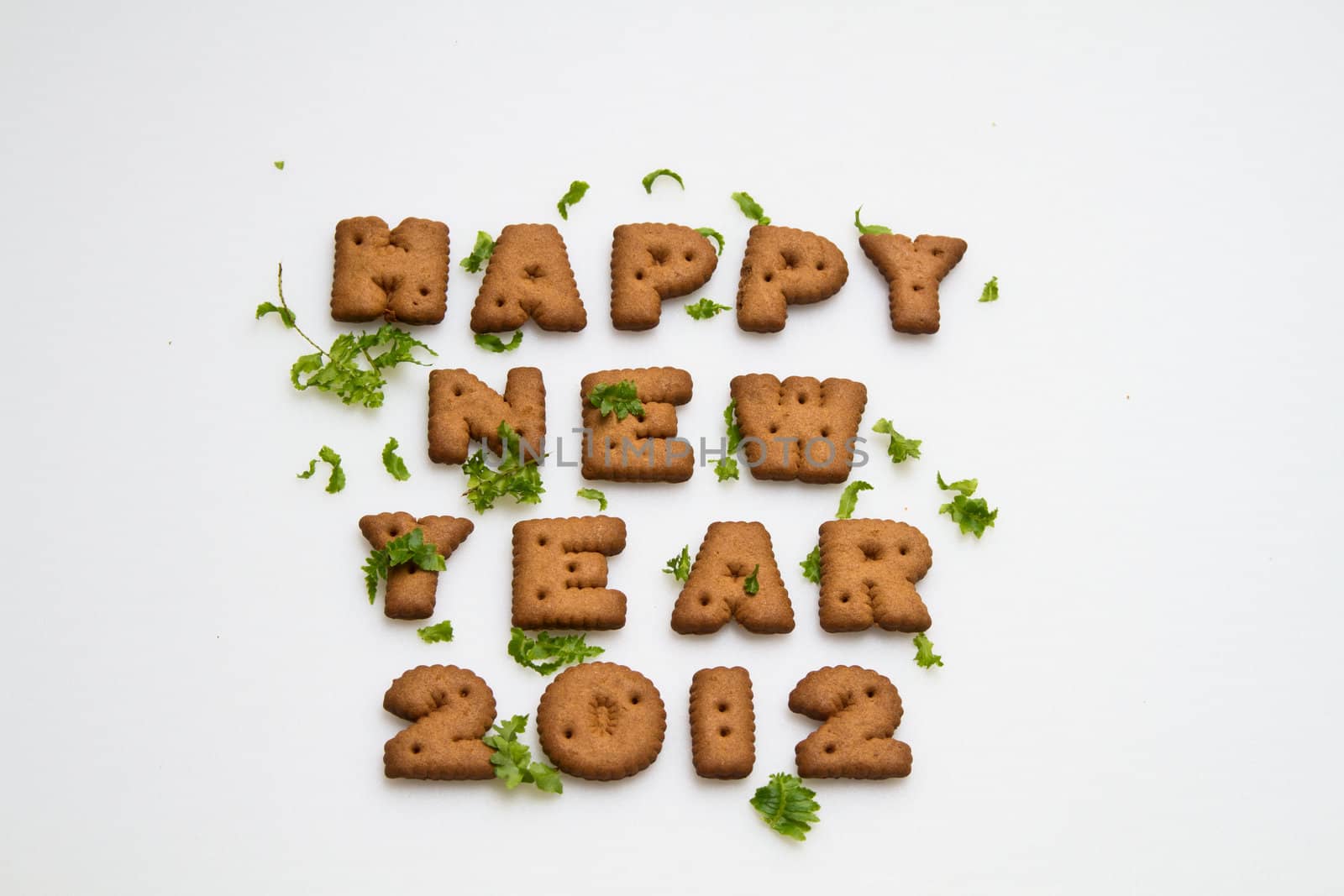 Happy New Year 2012 greeting words made by brown biscuits with green leaves on white surface in landscape orientation for background use