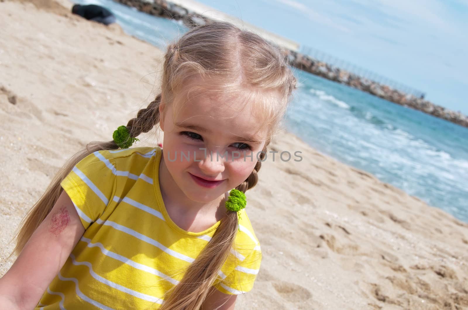 Little girl in yellow t-shirt sitting on the beach