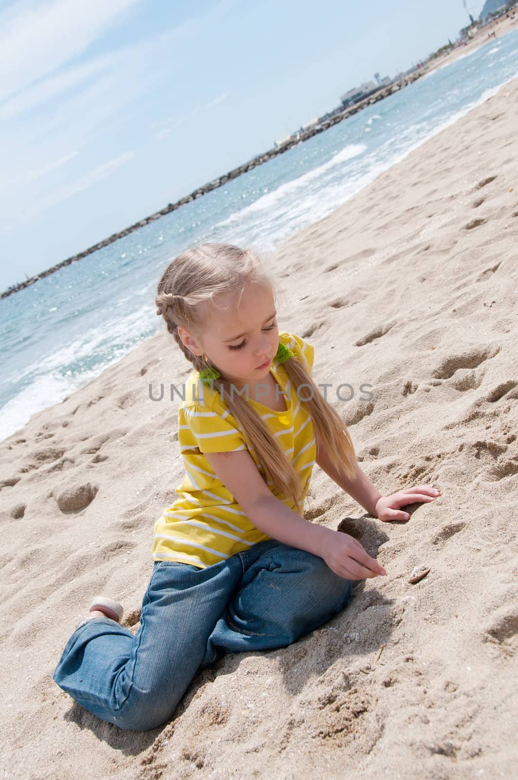 Little girl in jeans sitting on the beach