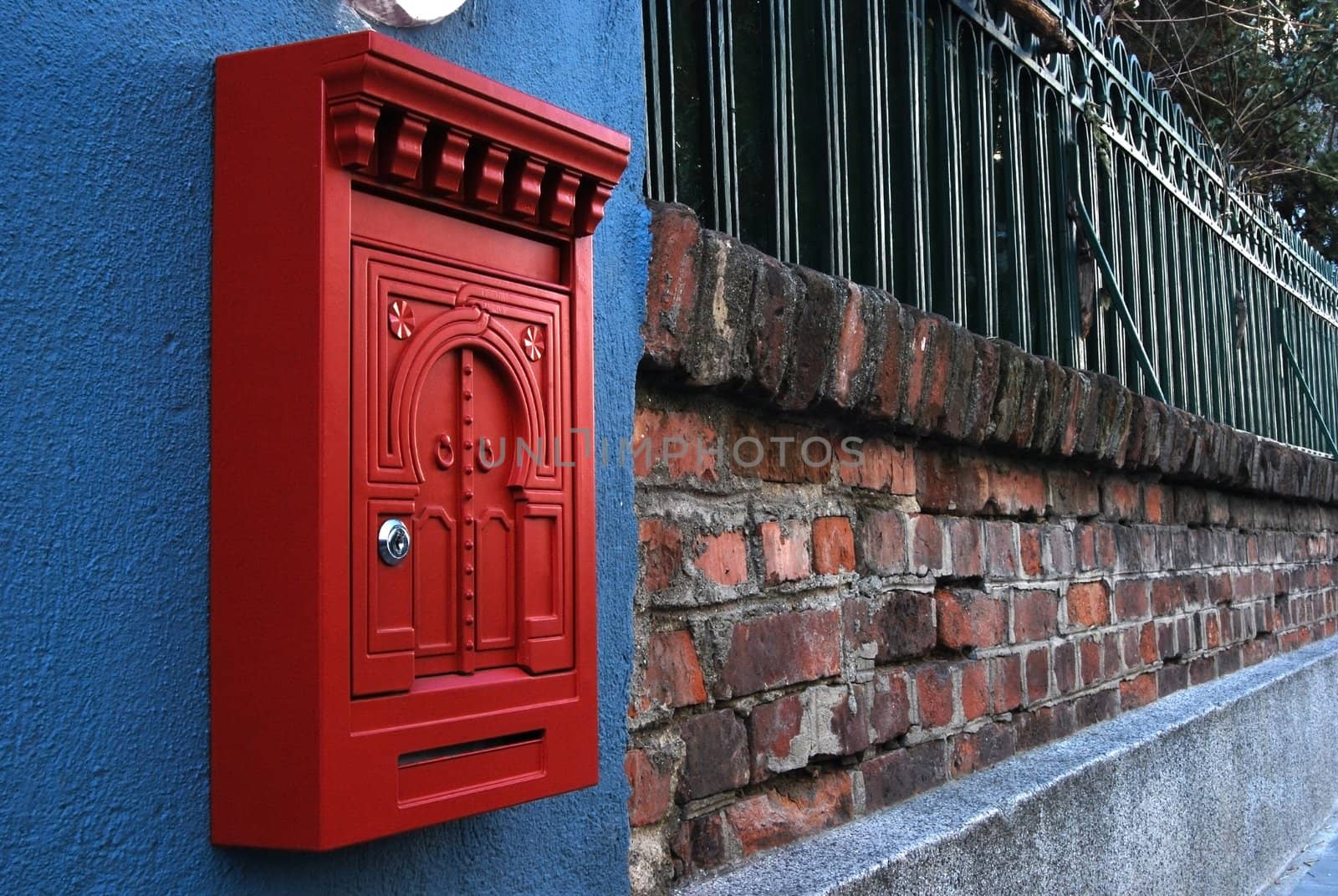 Red metal post box on brick wall and iron fence