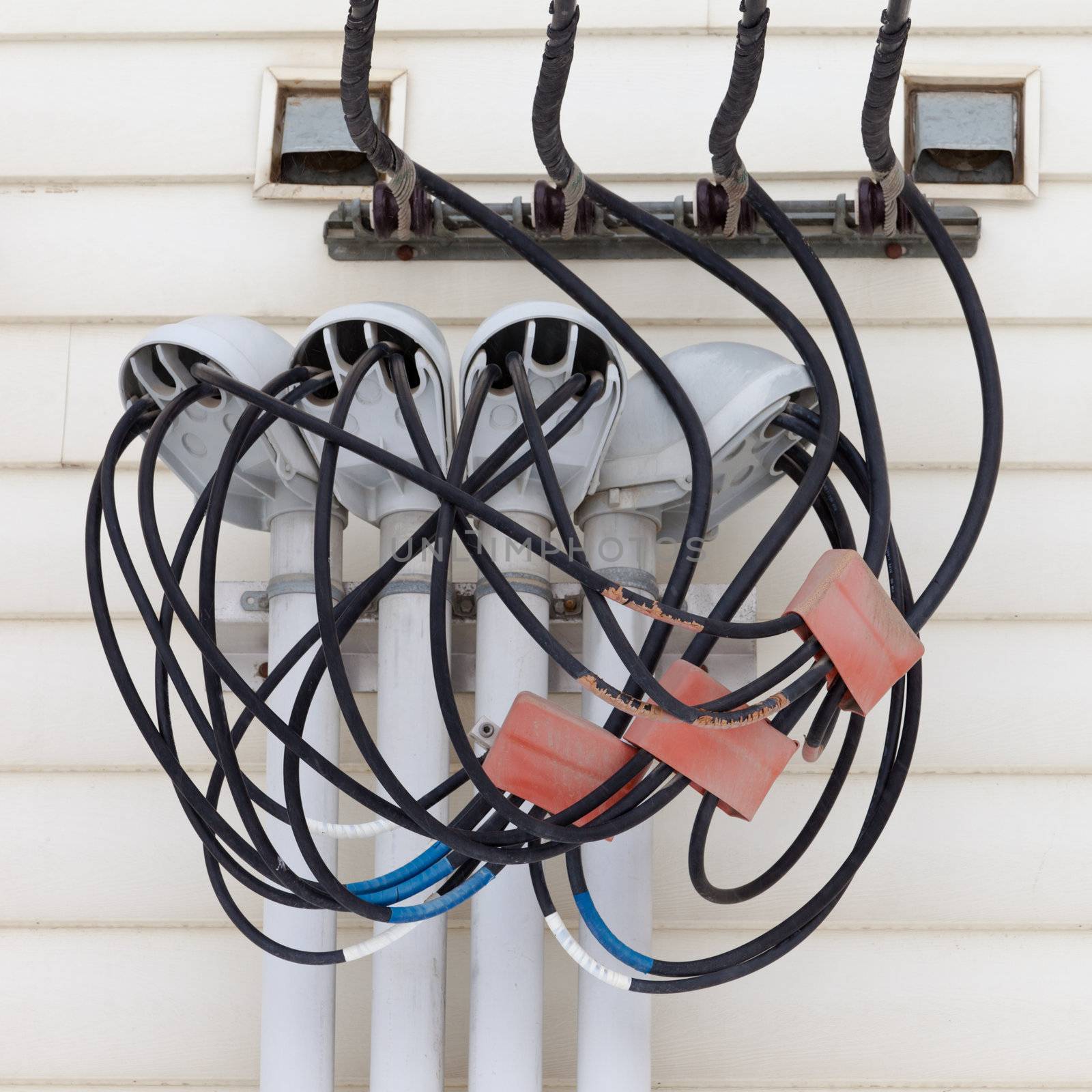 Incoming electricity supply with a complicated junction of wires and connectors on the exterior wall of a building with wooden siding