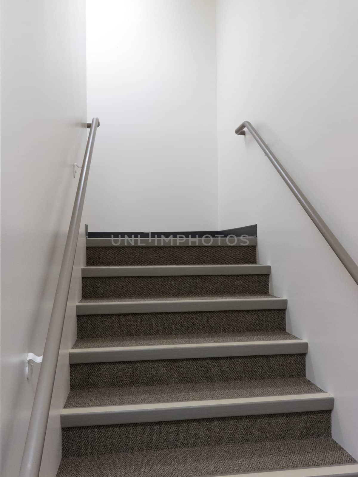 Looking up a flight of stairs in a well lit building with safety bannisters on either side