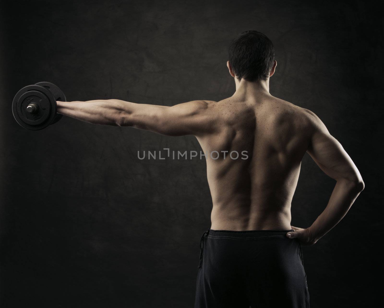Muscular male athlete is training by lifting dumbbells