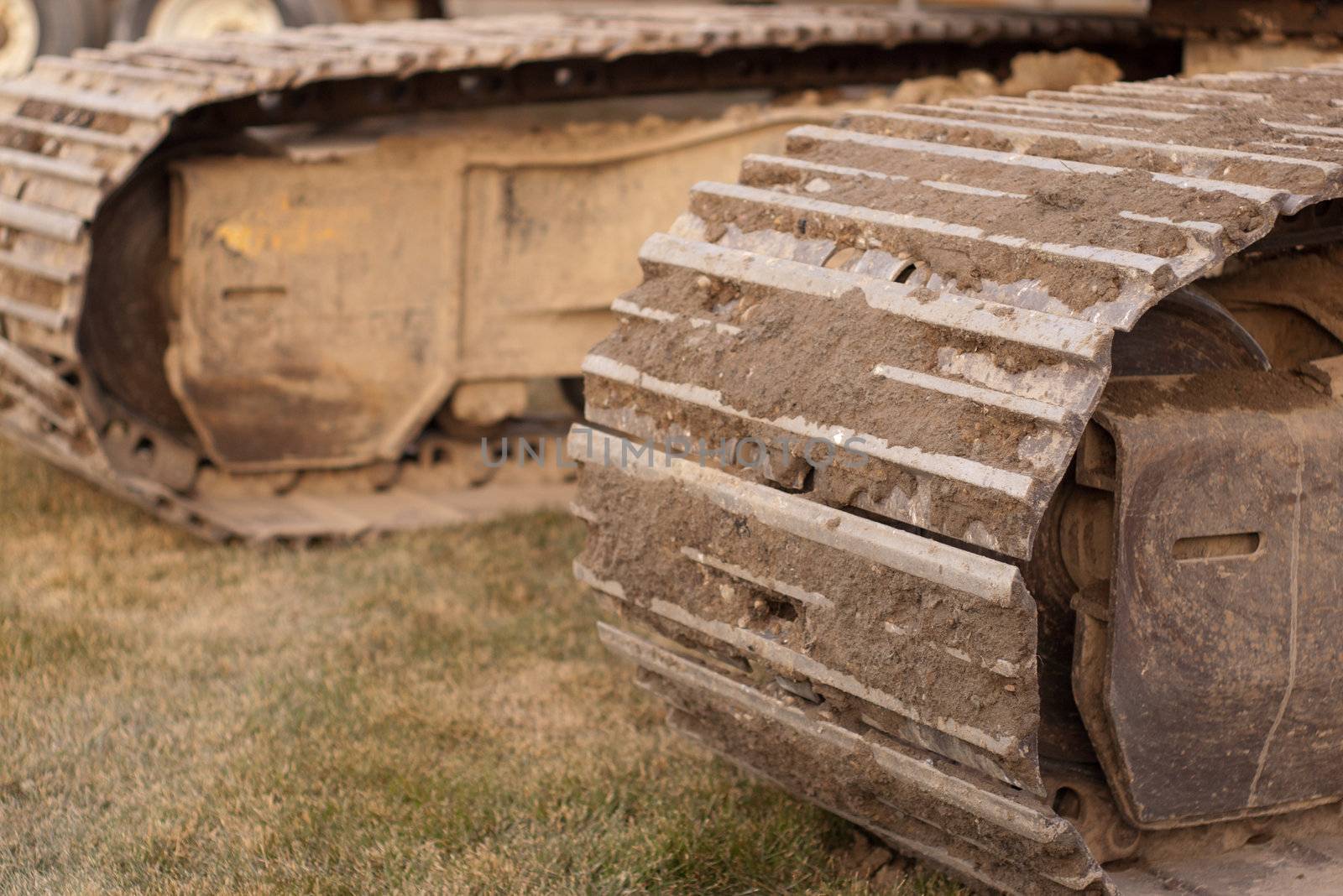 track of an excavator sitting on grass with dirt in the tracks