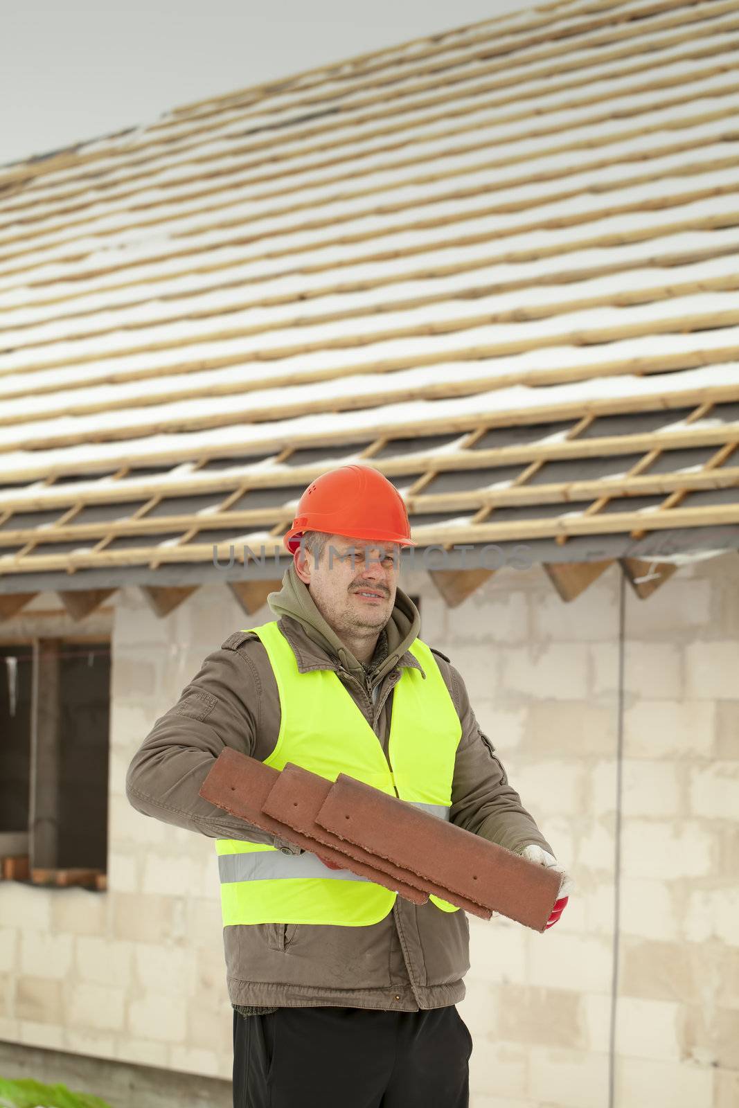 Builder with roof tiles near new building by A.L.
