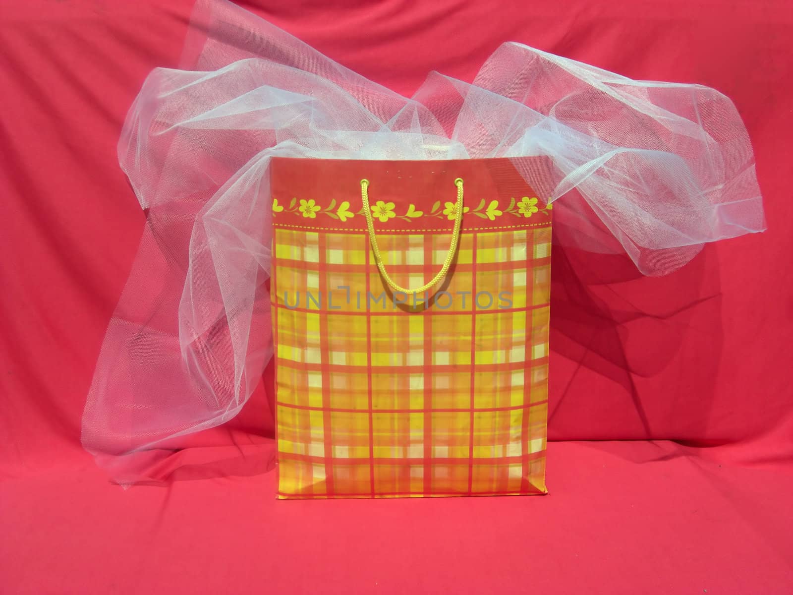 A colorful and large shopping bag is sitting on a cloth and a white veil is overlapping.