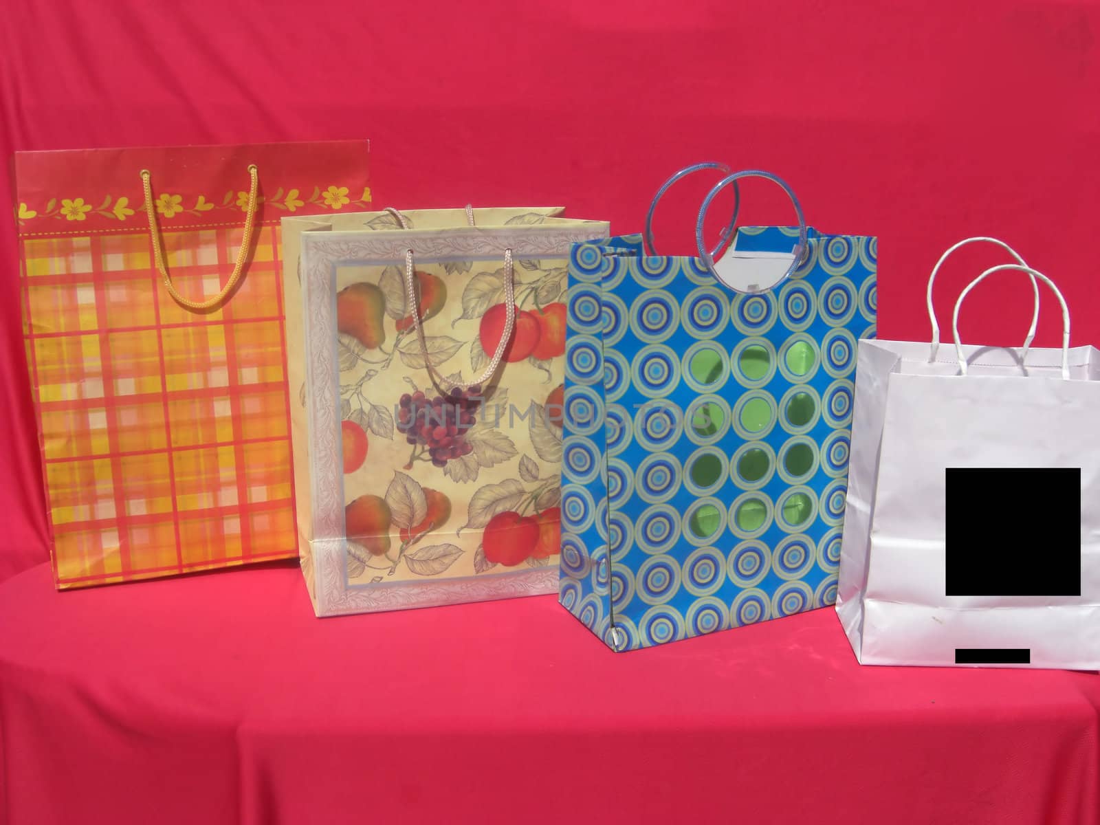 Four differently colored and sized shopping bags are on a red cloth.