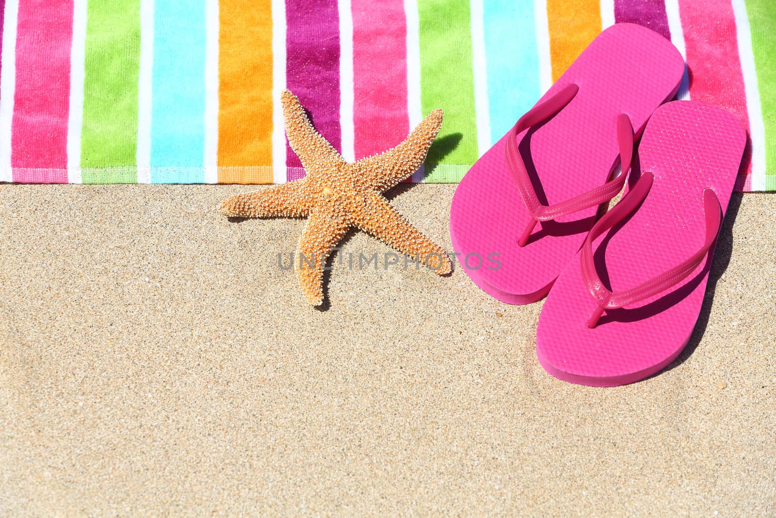 Tropical beach vacation holiday and travel concept with a colourful striped beach towel and vibrant pink sandal flip flip thongs on pristine sand with a starfish at an idyllic coastal beach resort.