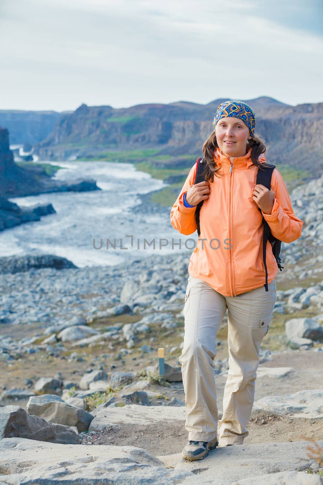 Cute woman hiking in the canyon Dettifoss waterfall in Vatnajokull National Park, Northeast Iceland. Vertical view