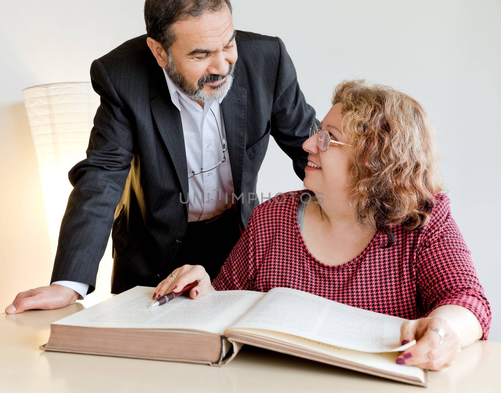 Happy adults behind book, looking at each other and smiling
