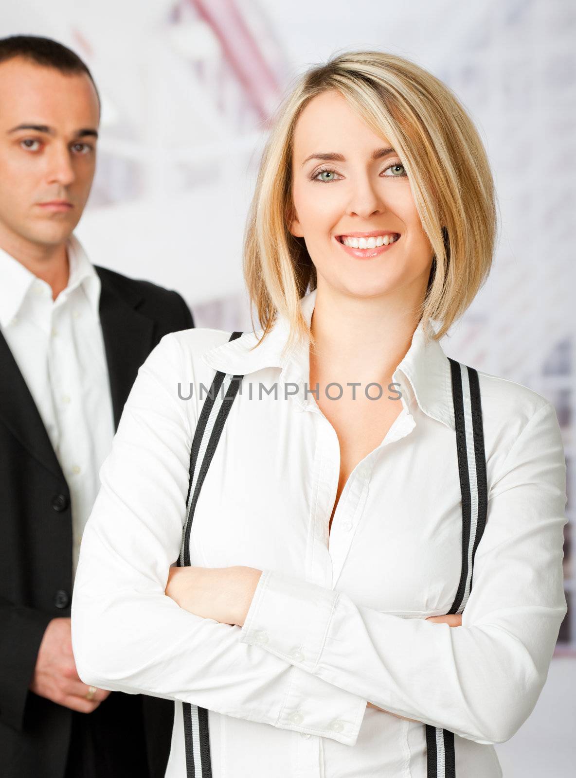 Young business couple - smiling woman and serious man in back, focus on female