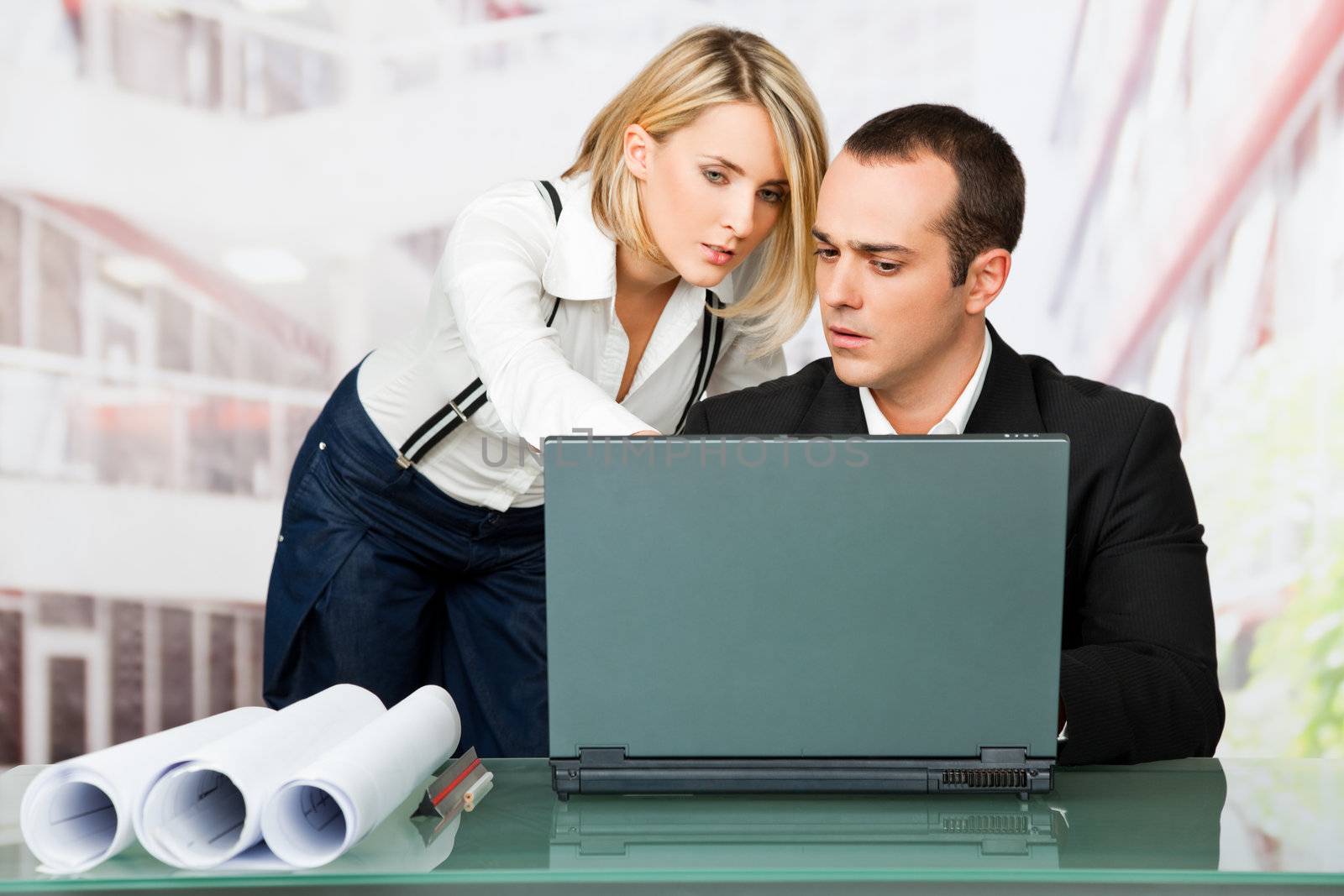 Male and female architects discussing behind laptop and blueprints