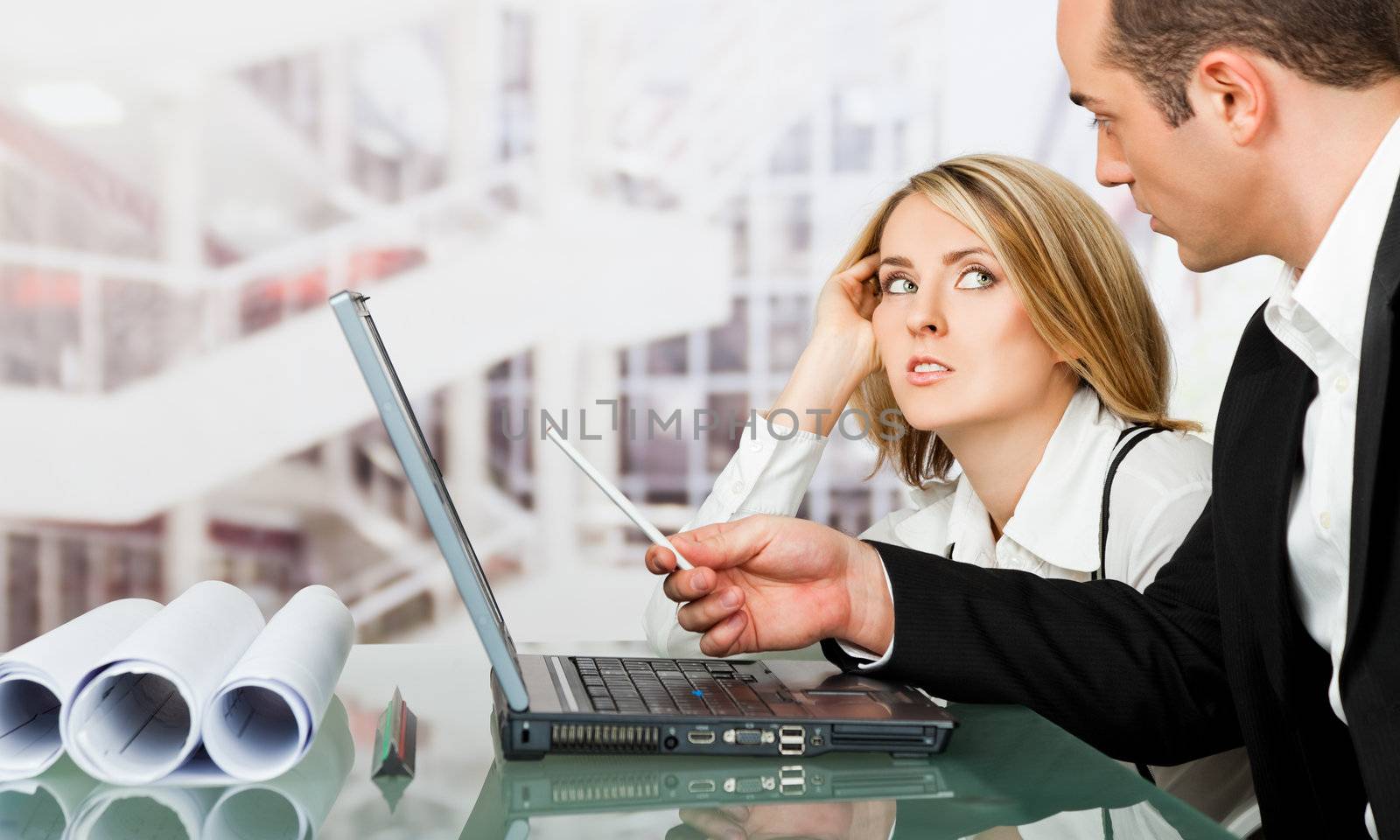 Male and female architects discussing work behind laptop, looking serious