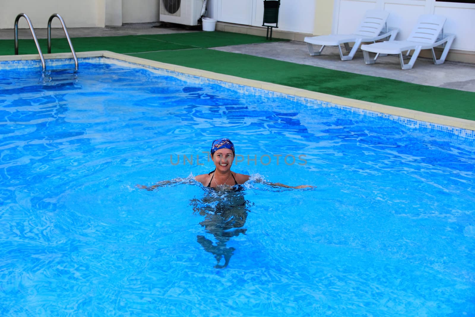 Beautiful young smiling girl sailling in pool in blue kerchief