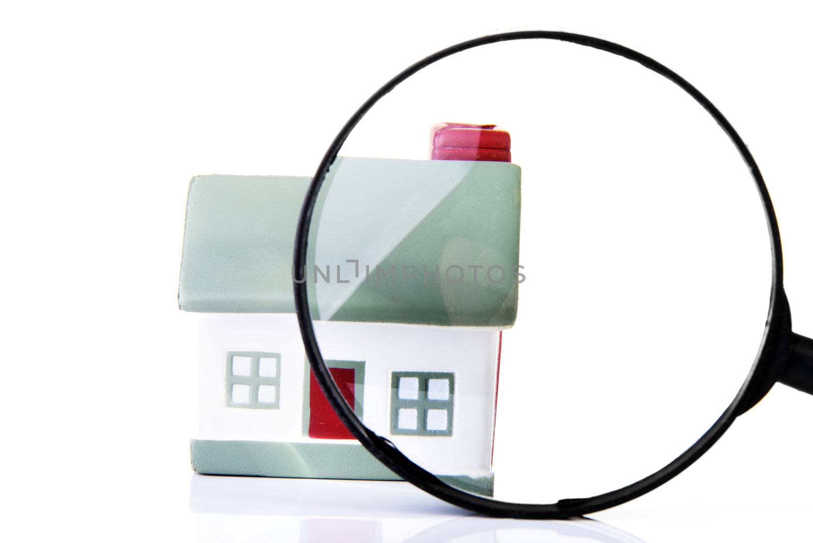 Magnifying glass inspecting a model single home building structure. Isolated on white. Real estate search concept.