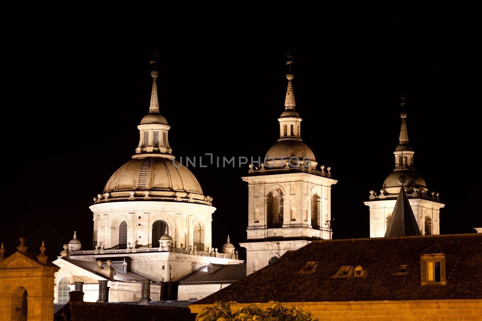 San Lorenzo de El Escorial Monastery  at night beautifully illuminated. Four towers are set off by black background.