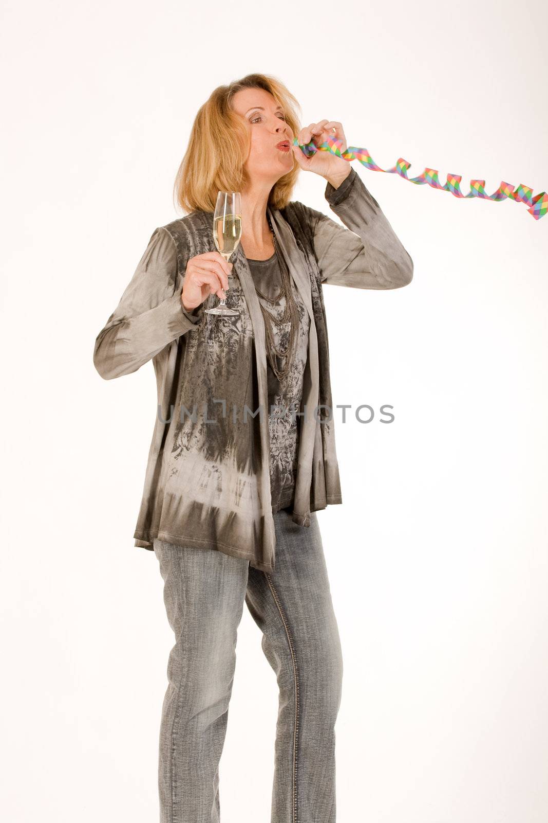 older woman blows out a streamer and has a glass of champagne in hand