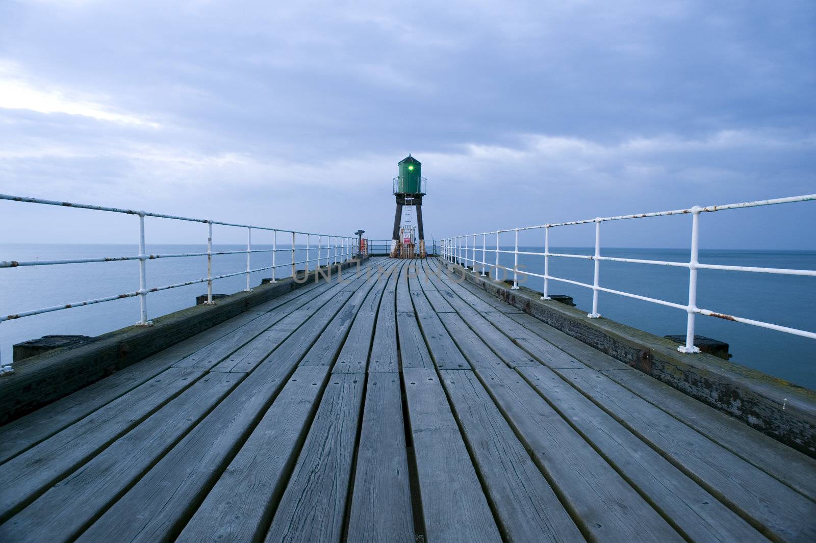 View along the deserted wooden planking forming the promenade on top of the pier or breakwater at the harbour entrance in Whitby to the navigation beacon at the end