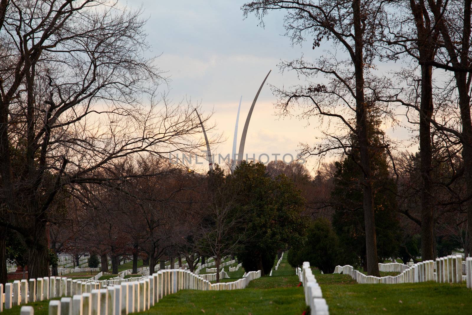 Christmas wreaths on gravestones in Arlington National Cemetery. Air Force memorial soars in the distance as the sun sets at dusk