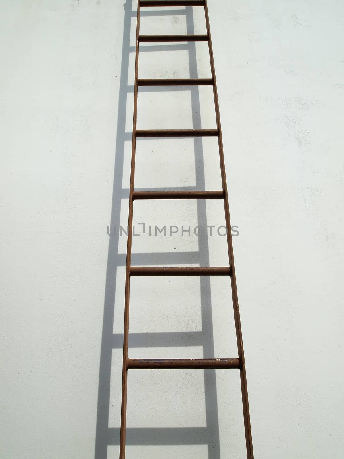 Brown iron ladder on white wall with shadow