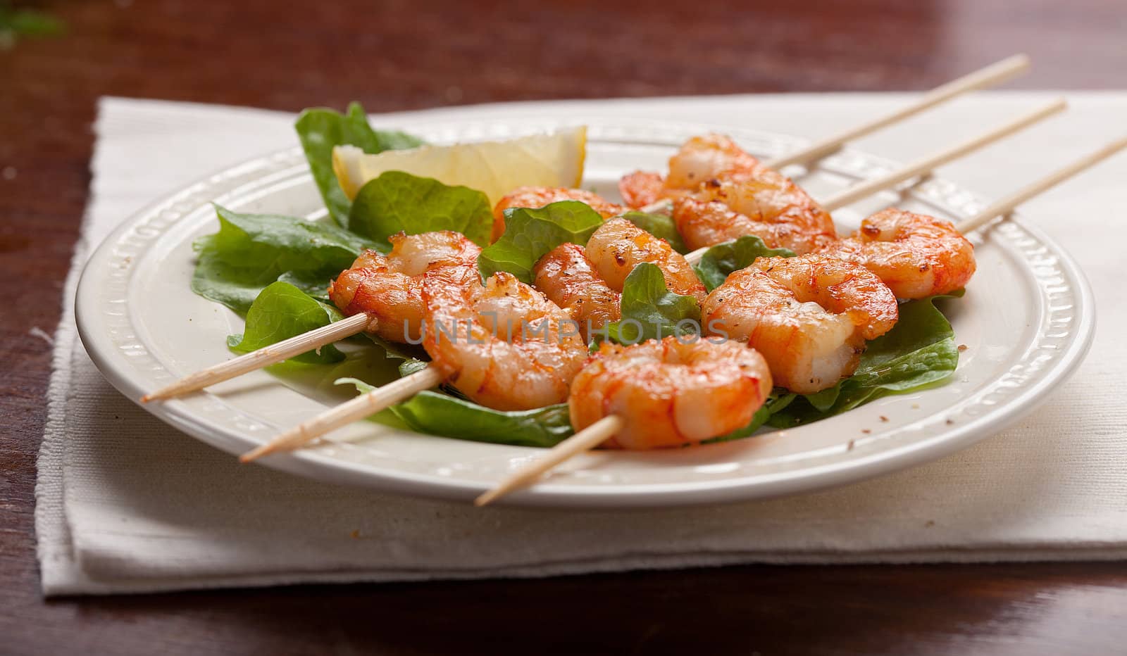 Roasted shrimps on the skewers with lettuce and lemon on the white plate