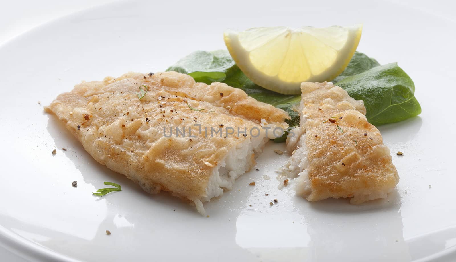 Fried fillet of tilapia with lettuce and lemon on the white plate