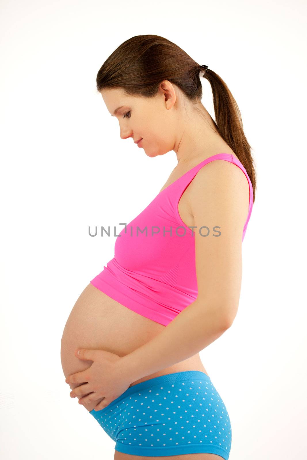 Pregnant belly. Healthy pregnant women in pink shirt and blue shorts holding her round berry with hands. White background.
