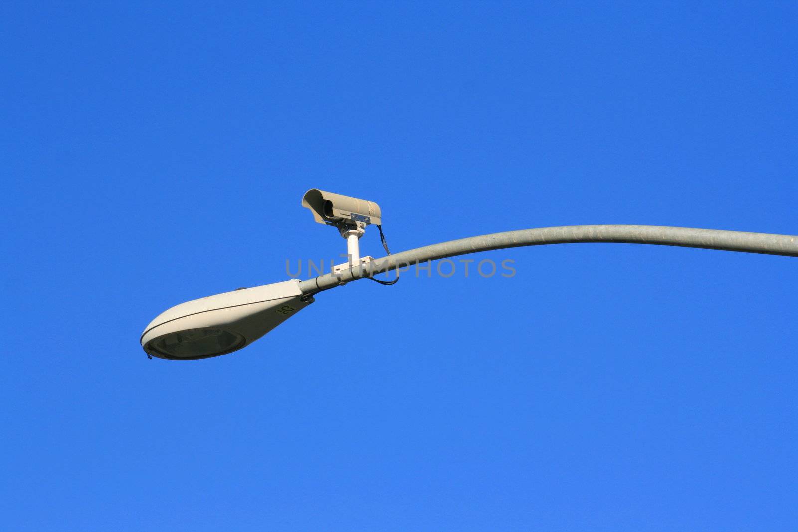 Surveillance camera on a light pole over blue sky.