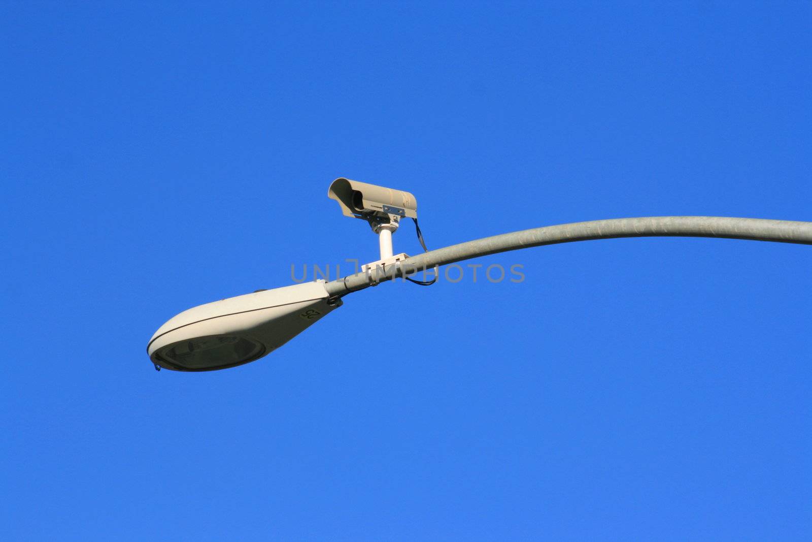Surveillance camera on a light pole over blue sky.