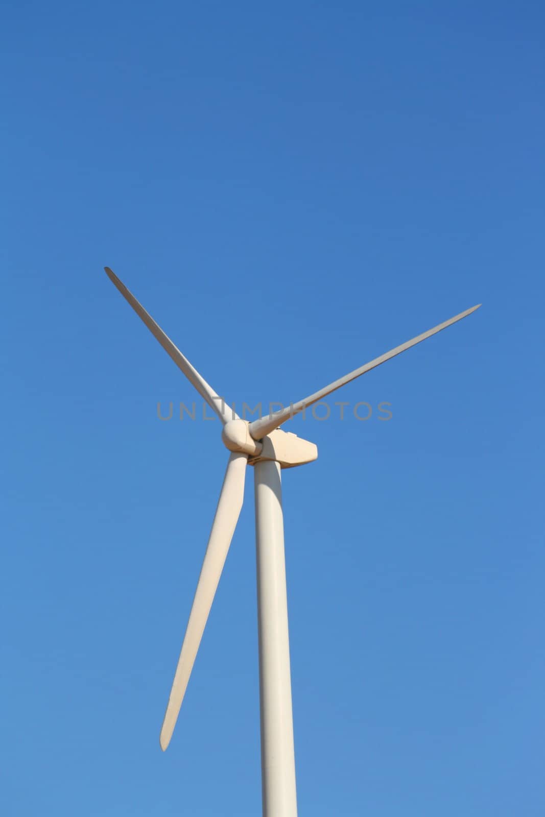 Close up of a wind turbine over blue sky.
