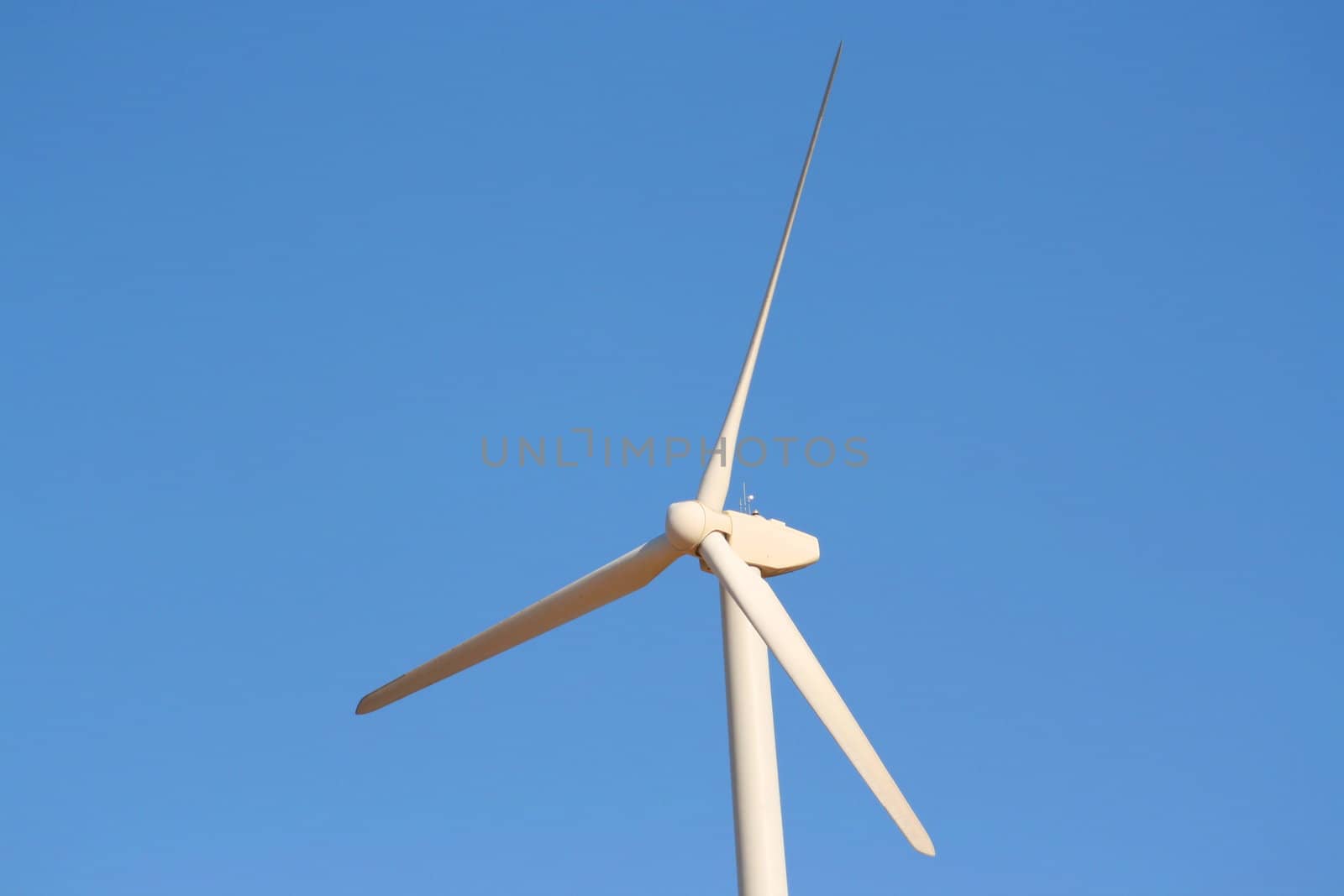 Close up of a wind turbine over blue sky.
