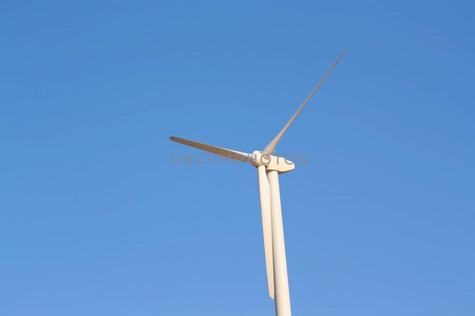 Close up of a wind turbine over blue sky.
