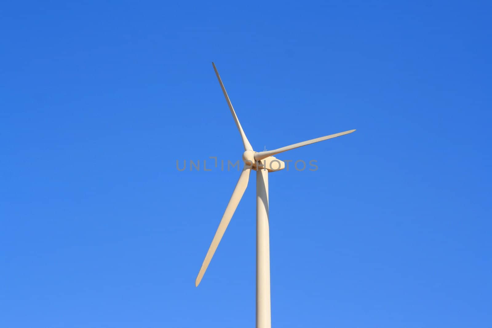 Close up of a wind turbine over blue sky.
