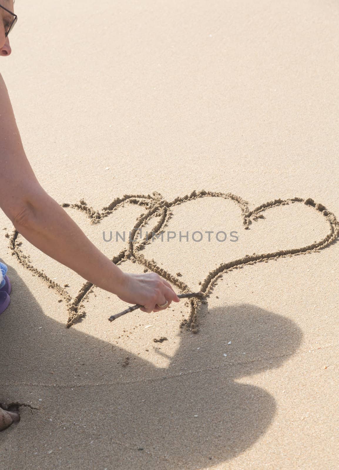 Lady drawing pair of linked hearts in sand on beach in Caribbean