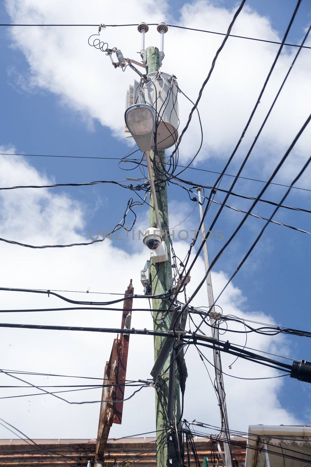 Complicated wiring forms tangled mess on power pole with light and camera