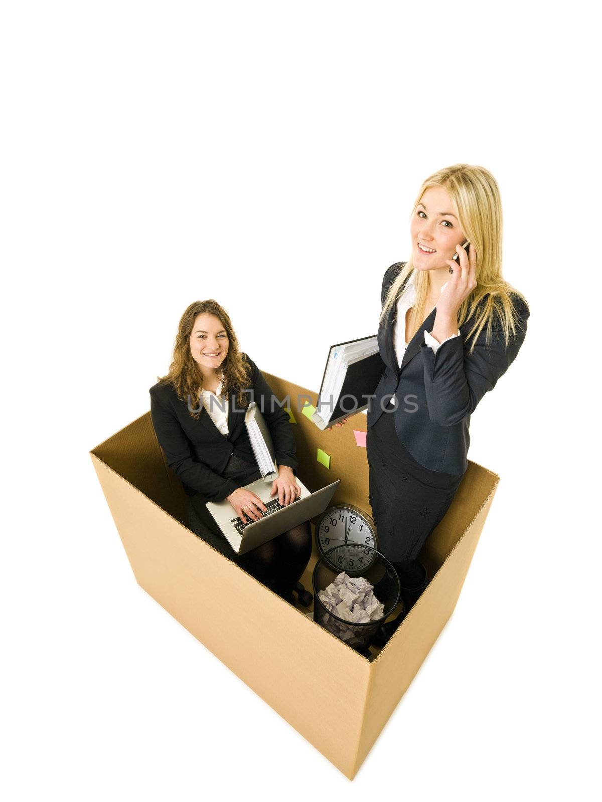 Two Business women in a very small Cardboard office isolated on white background