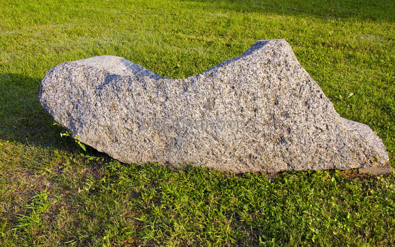 Large decorative stone on the grass in the garden illuminated by the sun.