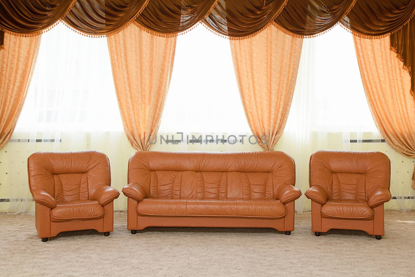Leather armchairs and a sofa. The interior with curtains