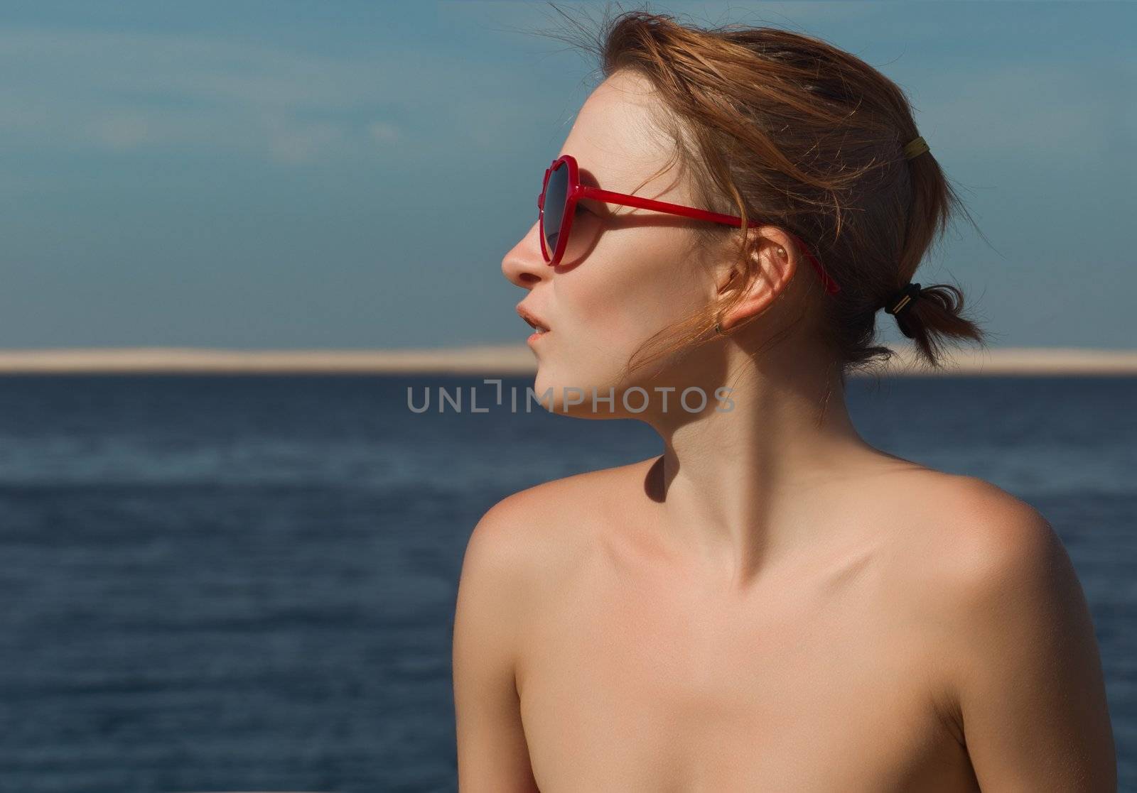Young red woman wearing sunglasses with sea at background