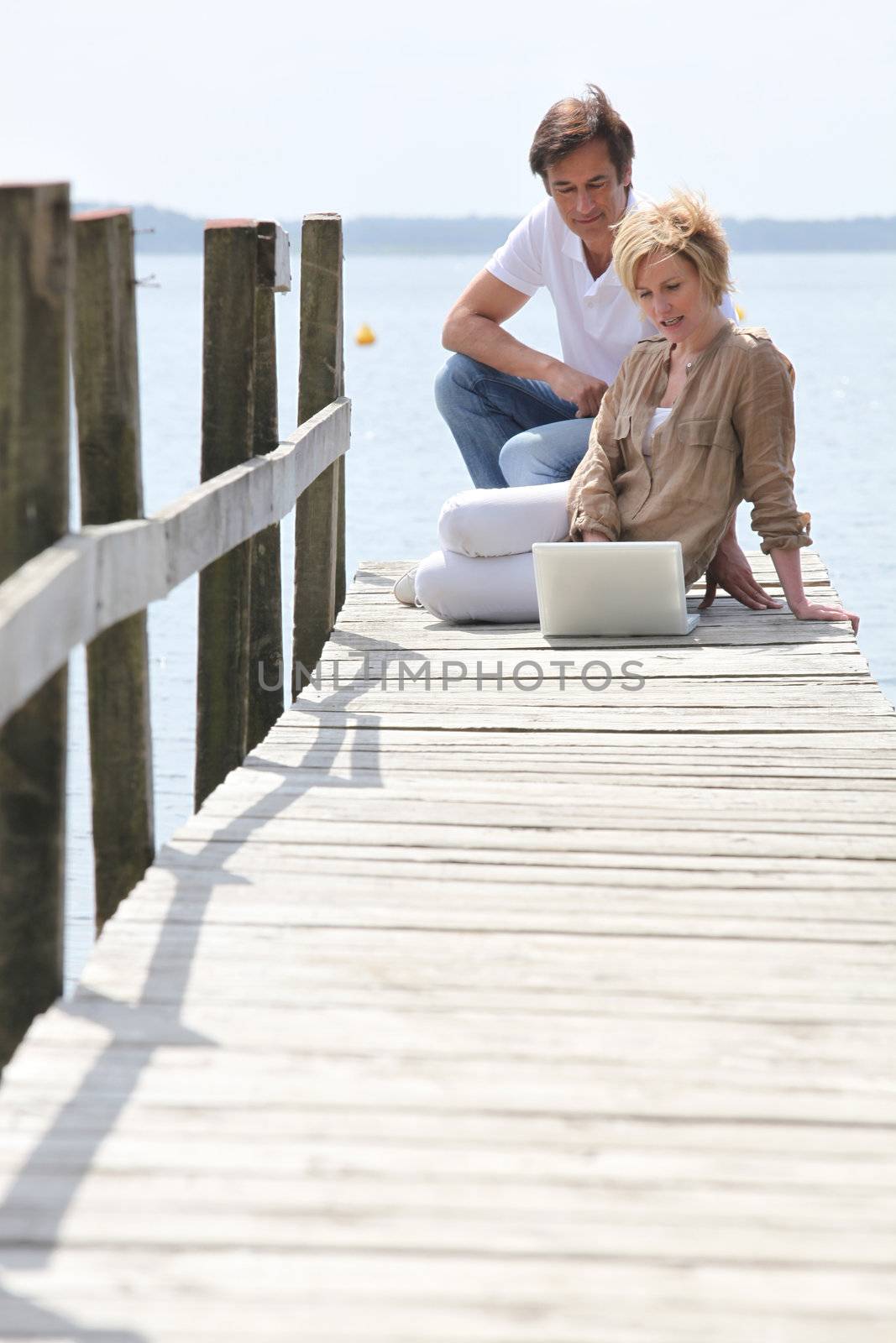 mature couple with laptop seated on pontoon by phovoir