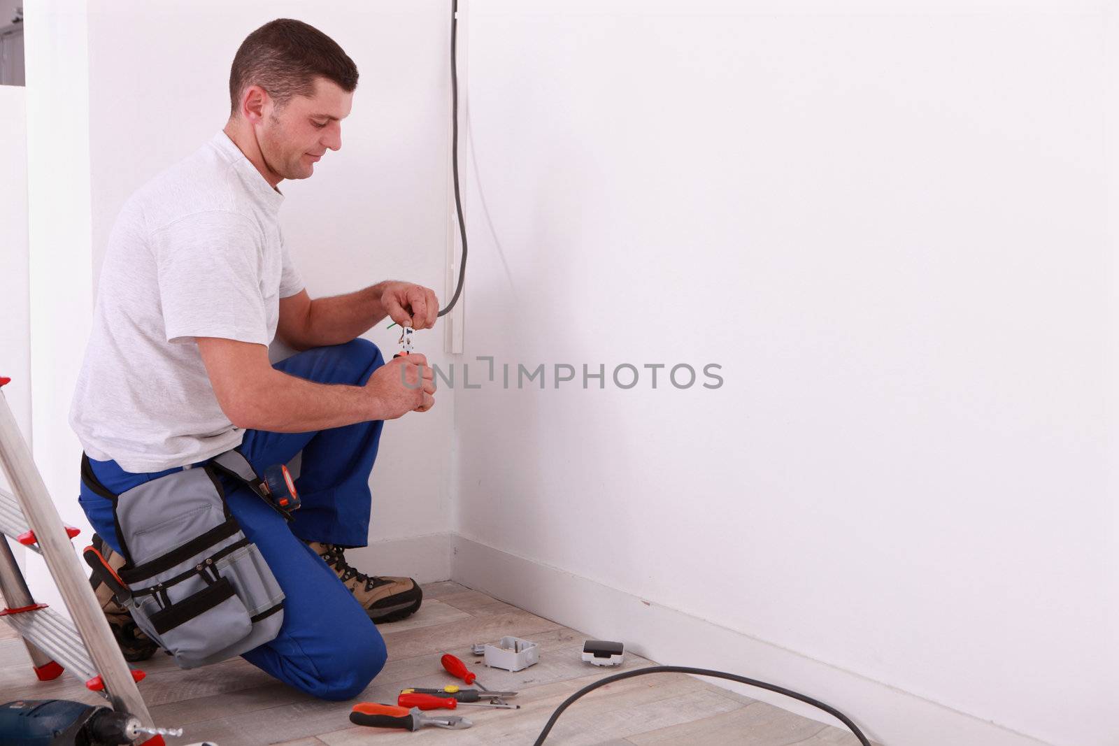 Male electrician preparing length of wire by phovoir