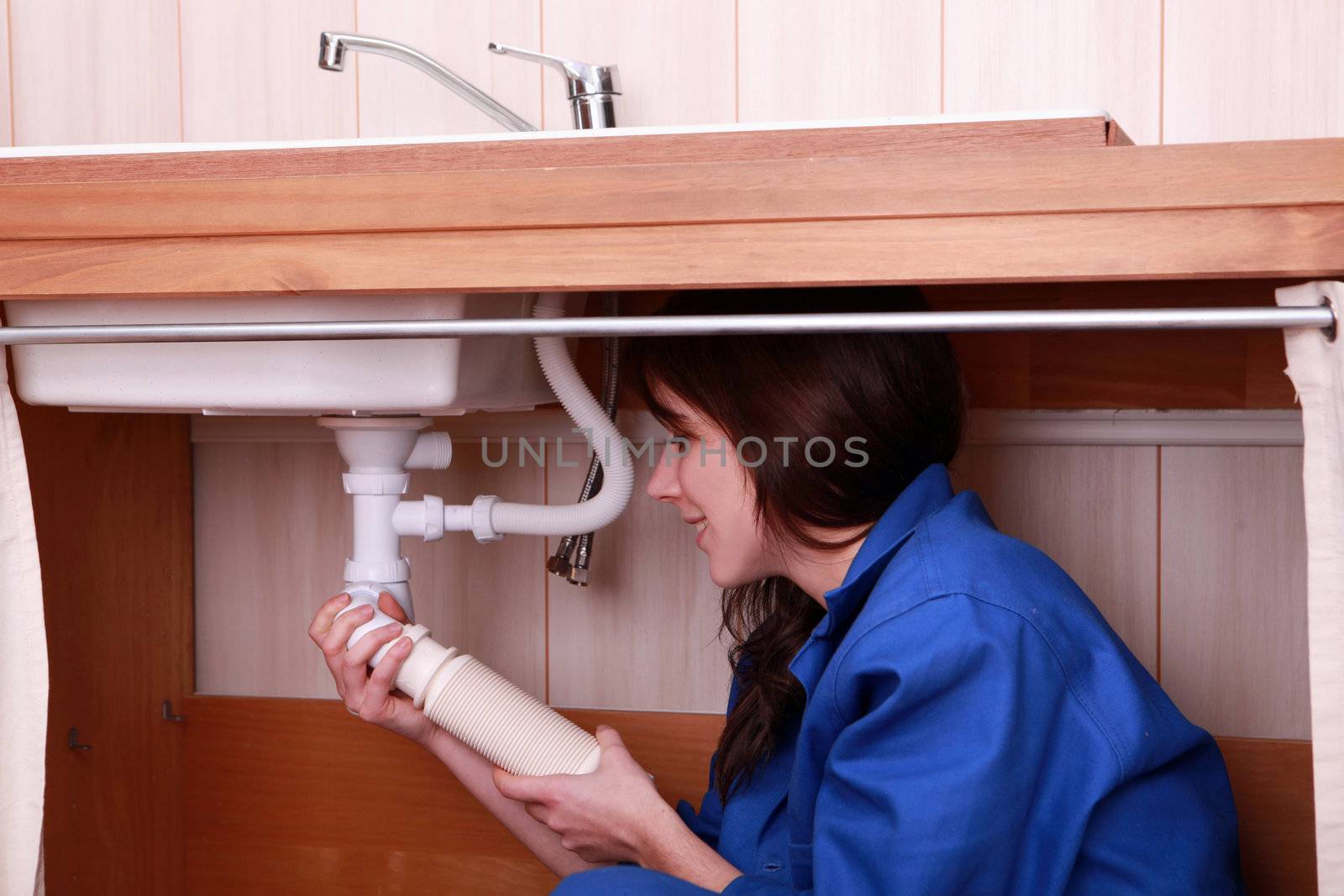 Young female apprentice plumbing a sink by phovoir