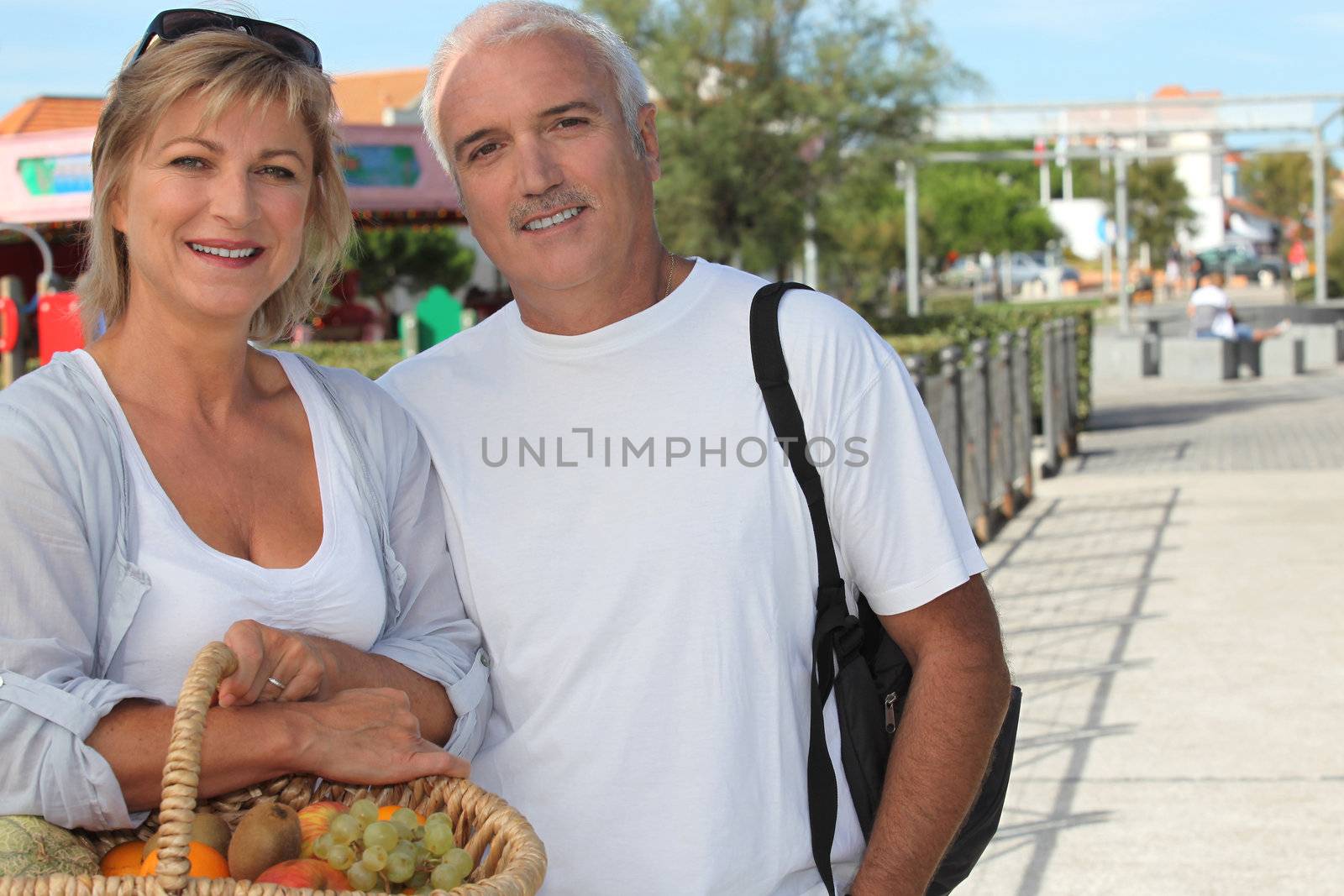 Couple on holiday with a basket of fruit by phovoir