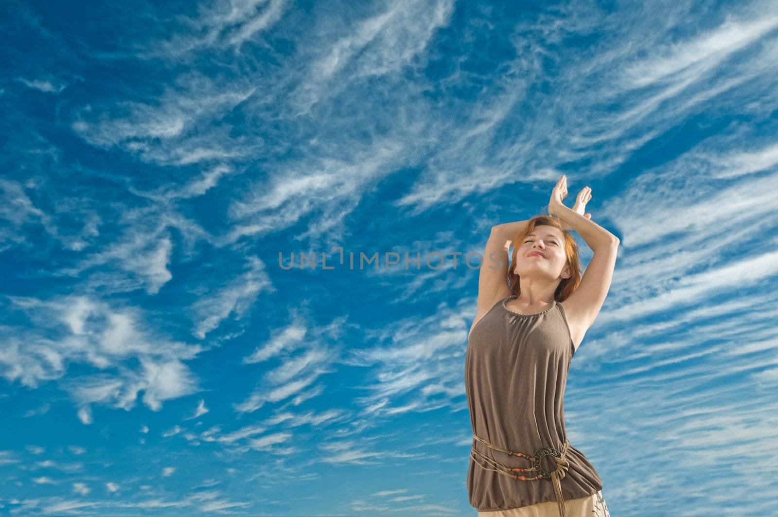 Beautiful young dancer performing yoga-dance outdoors with blue sky and clouds in the background