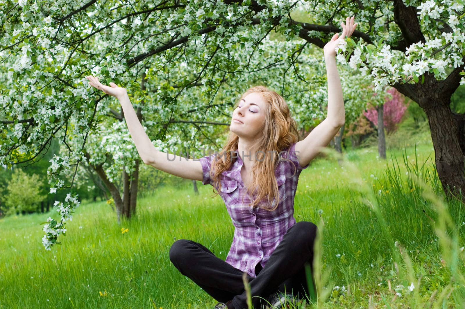 Red-headed woman meditating under blooming tree