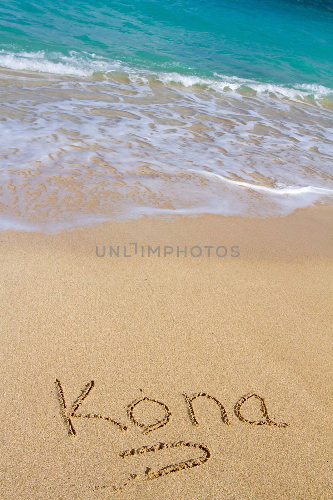 This vacation image shows the word Kona written in the sand with the Ocean water waves coming in to wash the writing away.