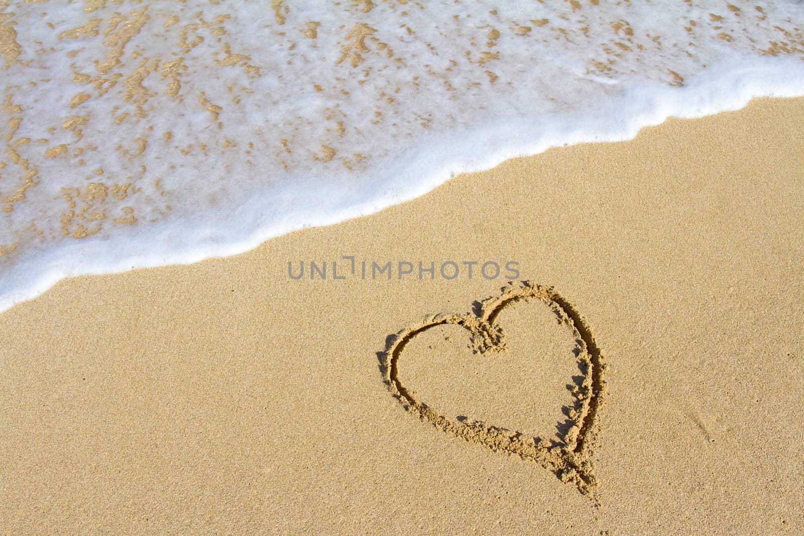 A heart is drawn in the sand on the Hawaii beach showing an image of white sand, water, waves, and the symbol for love. This would be a great image for a honeymoon, valentines day, or any sort of love design that needs a tropical vacation look.